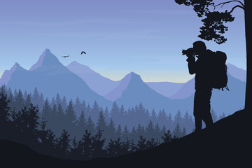 A tourist photographing a flying bird in a mountain landscape with forest under a morning sky with dawn and clouds