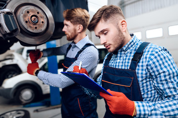 Father and son work at the auto service. Two mechanics work with the details of the car.