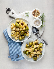 two plates with Italian gnocchi from potatoes with Brussels sprouts and walnuts on a white marble cutting board on a stone kitchen table. classic healthy recipes