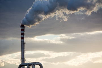 Smoking Red and White Bands Chimney On Backlight With White Smoke At Sunset