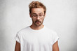 © wayhome.studio - Curious intelligent male wears round spectacles, casual t shirt, notices something down, concentrated on floor, has puzzled look, isolated over white studio background. People and facial expressions