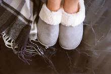 Female Legs In Cozy Slippers On Mramor  Floor With Cashmere Blanket. Woman Wearing  Warm And Comfortable Slippers On The Morning. Relax And Stay At Home Concept. Copy Space.