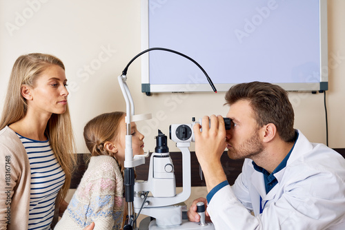 Cuadros en Lienzo Side view portrait of cute little girl looking at slit lamp machine during medi