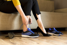Woman Changing High Heels, Office Shoes After Working Day While Sitting On The Couch, Ready To Take A Walk Or Run