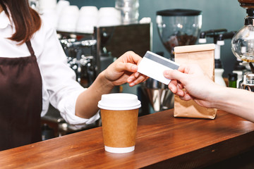 Female barista  taking a credit card from customer in coffee shop