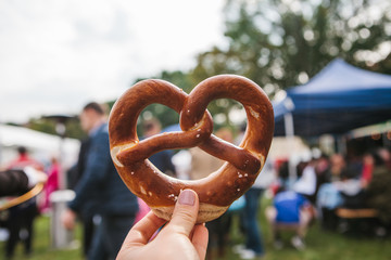 Celebration of the famous German beer festival Oktoberfest. The person holds in his hand a traditional pretzel called Brezel in the background of a blurry people.