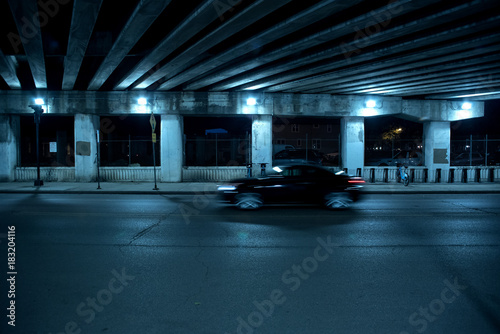 Cuadros en Lienzo Gritty dark Chicago highway bridge and city street with a passing black car and bicycle stand at night