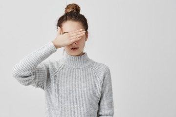 Wall Mural - Skinny woman wearing grey outfit closing her eyes with hand. Confident female trying to hide her face from other people prefer not to see. Decision, human concept