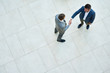 © Seventyfour - Top view of two business people shaking hands standing on tiled floor in hall of modern office building, copy space