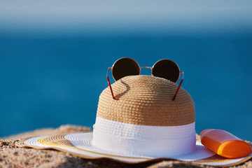 Bonnet hat, sunglasses and bottle of sunscreen against the sea.