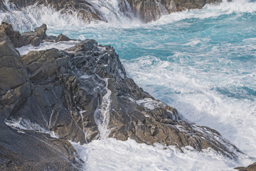 Wall Mural - Sea foam whitens rocks.