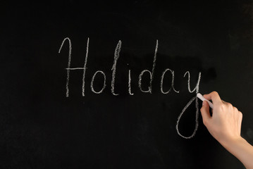 Woman hand write word Holiday on school blackboard with white chalk