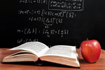 Book and Apple on wooden table in front of blackboard where is mathematical equation in the classroom