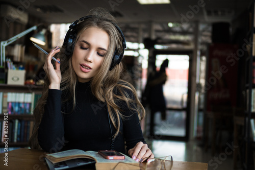 Fotografia, Obraz Female student sitting on the library and singing while listening to loud music