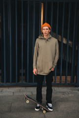 Skateboarder in oversized hoody with board standing in front of metal fence