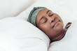 © mavoimages - Young African woman wearing a headscarf asleep in bed