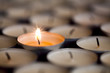 Selective focus on magical light from a single sparkling flame from one candle among many extinguished tealight candles.