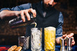 Elegant bartender pouring fresh orange vodka cocktail over ice in crystal glassware