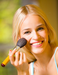 Young blond woman with makeup brush at home