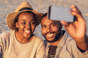 Wall Mural - Content young African couple taking selfies together at the beach