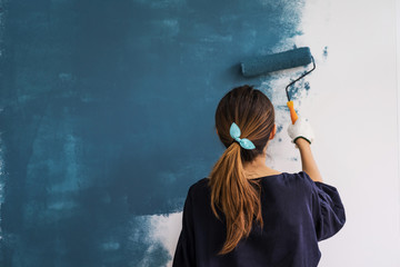 young asian happy woman painting interior wall with paint roller in new house, home decoration conce
