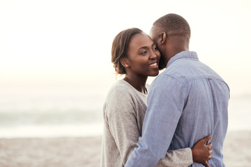 Wall Mural - Young African woman embracing her husband at the beach