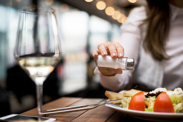 Woman adding salt to food in restaurant.