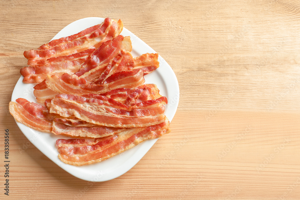 Plate with cooked bacon rashers on wooden table