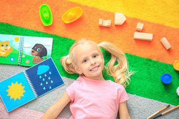 Canvas Print - Cute little girl with toys on color carpet in kindergarten