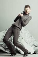 Strike A Pose, Haute Couture Concept. Full Length Portrait Of Androgynous Model With Short Hair Holding Lapels, Posing Over Gray Background. Pale Skin, Natural Make-up. Futurism Style. Studio Shot