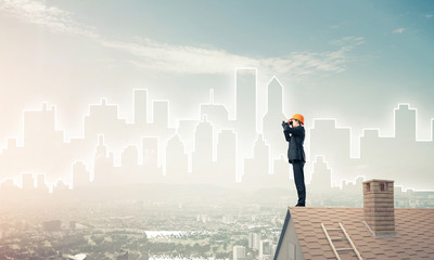 Engineer man standing on roof and looking in binoculars. Mixed m