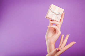 Female hands holding a small gift box on violet background.