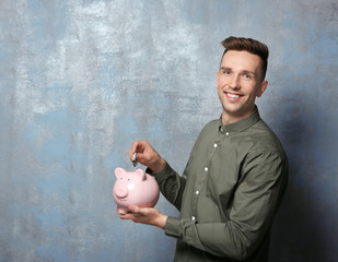 Poster - Young man putting banknote into piggy bank on grunge background