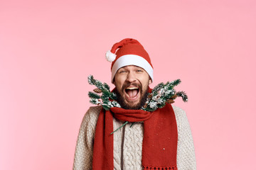 man with a beard in a New Year's cap smiling, artificial spruce branches in a scarf, light pink background, free space for copying, new year, christmas, holiday