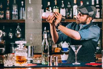 Wall Mural - Portrait of barman preparing cocktails, using shaker and pouring beverages