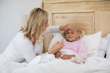 Wall Mural - Mother checking sick daughter temperature with digital