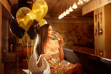 Glamour beautiful  smiling woman with champagne and golden ballons on background in a restaurant selebrating new year, christmas, x-mas