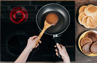 Wall Mural - cropped shot of woman flipping pancake on frying pan with wooden spatula