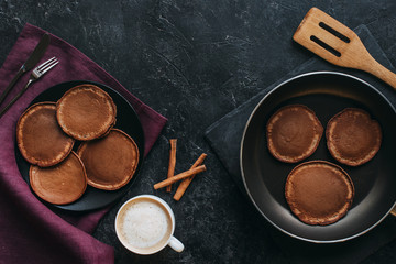Wall Mural - top view of coffee cup and tasty pancakes on plate and frying pan on black tabletop