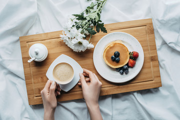 Wall Mural - cropped shot of woman eating breakfast with pancakes and coffee in bed