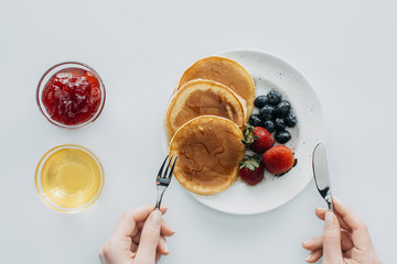 Wall Mural - cropped shot of woman eating pancakes with berries on white table