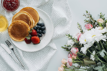 Wall Mural - top view of tasty breakfast with pancakes and flowers bouquet on white