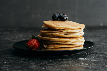 Wall Mural - stack of pancakes with blueberries and strawberry on black plate