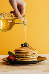 Wall Mural - cropped shot of person pouring maple syrup onto stack of pancakes