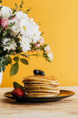 Wall Mural - stacked pancakes with berries and syrup on table with flowers in vase