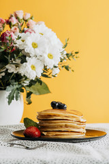 Wall Mural - delicious stacked pancakes with berries and syrup on table with flowers in vase