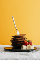 Wall Mural - delicious stacked pancakes pierced with fork on plate with fruits