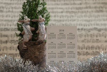 Calendar Of 2018 Year With Winter Festive Decoration & A Cute Couple Of Happy Bunnies Are On The Burred Background Of Sheet Music. New Year Holiday Card. 