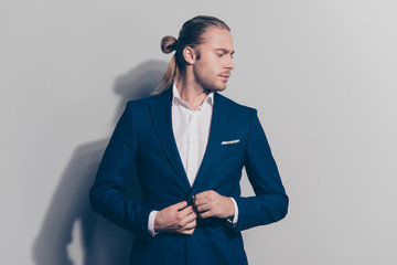 Side view face portrait of stylish, caucasion man correcting buttons on his blue jacket, turned face to the side with a serious expression, standing over  gray background