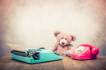 Wall Mural - Teddy Bear toy sitting at the old wooden desk with mint green retro typewriter and telephone circa 60s front concrete wall background. Vintage instagram style filtered photo
